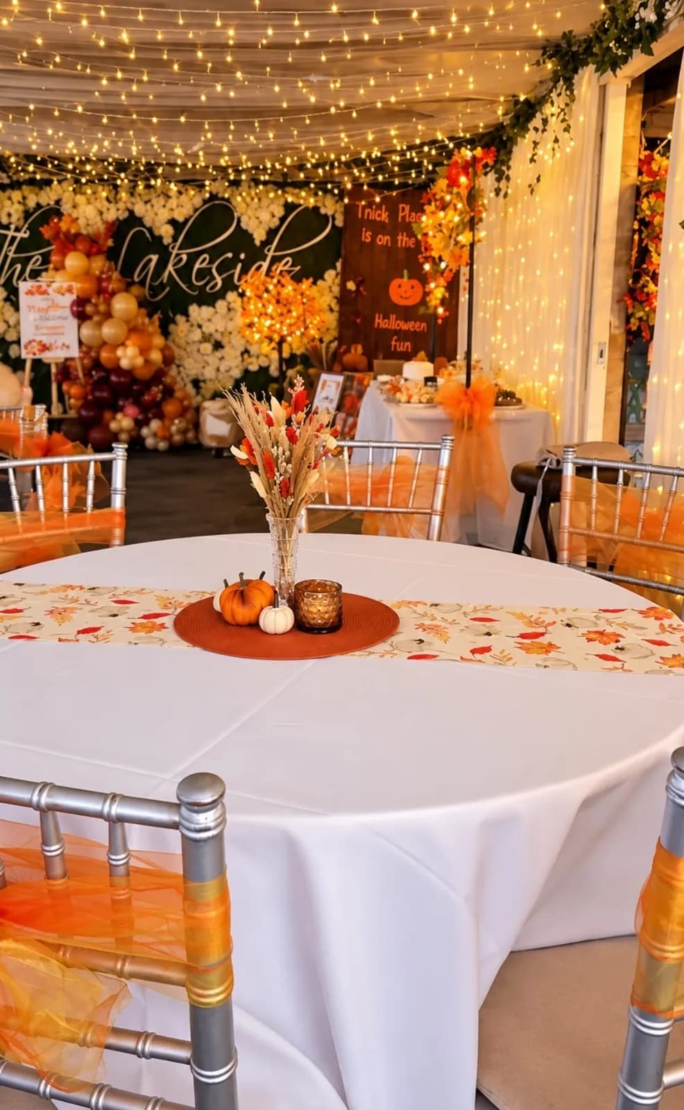 A round table dressed for an autumn party at The Lakeside, with pumpkins, orange chair sashes and fairy lights above